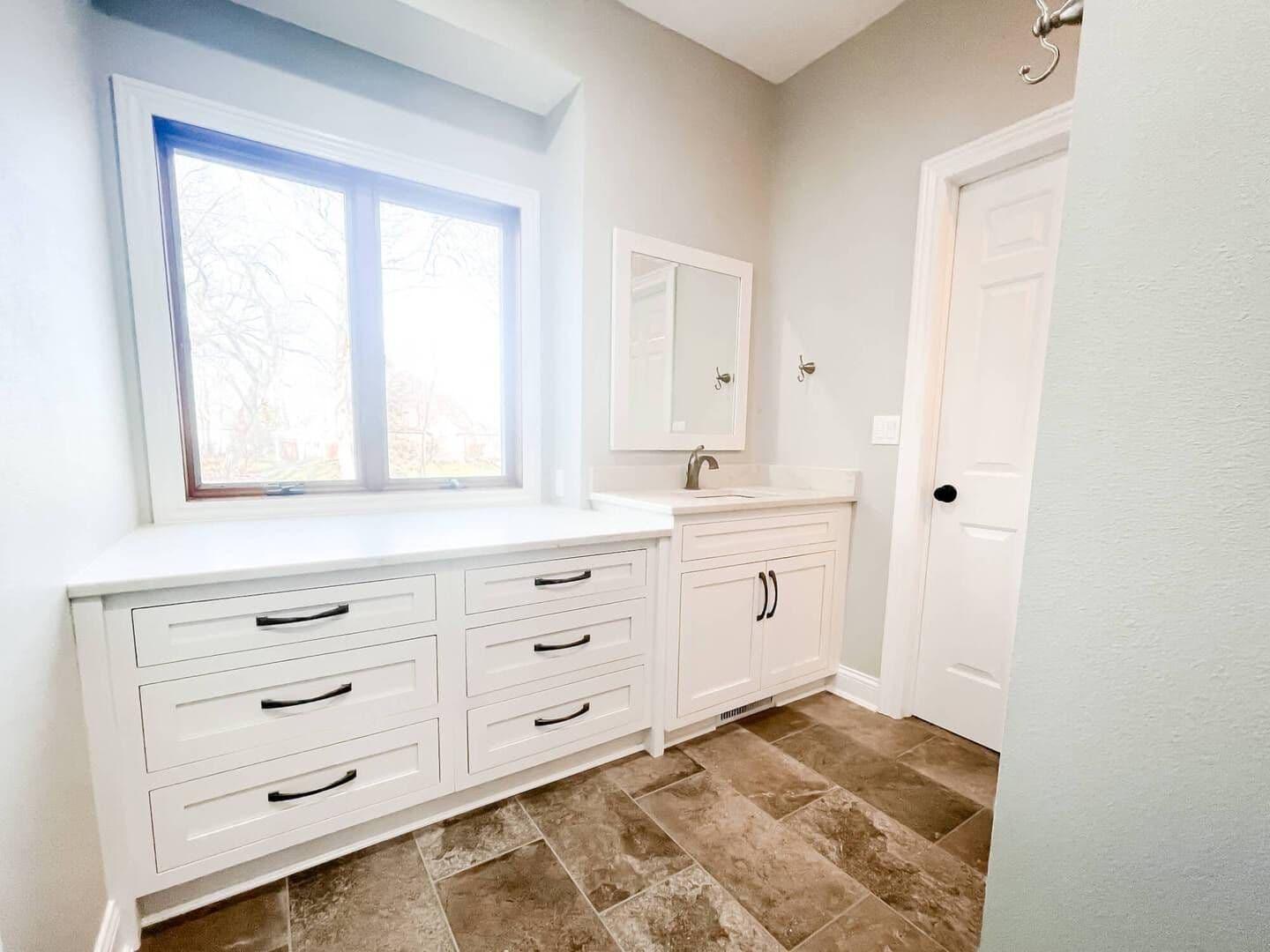 Large bathroom vanity with white cabinets and window