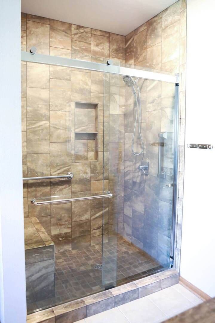 full view of shower with brown tile marbling, clear glass doors shut with silver fixtures