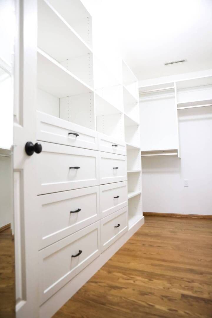 angled picture from ground and across showing white drawers with black pulls and white shelving units up to the ceiling on top