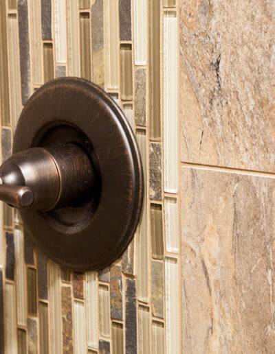 Close up of a brown shower handle and custom wall tiling