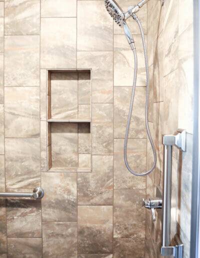 side view of silver shower fixtures (shower head, faucet and handlebars) with large brown marbled tiles along walls