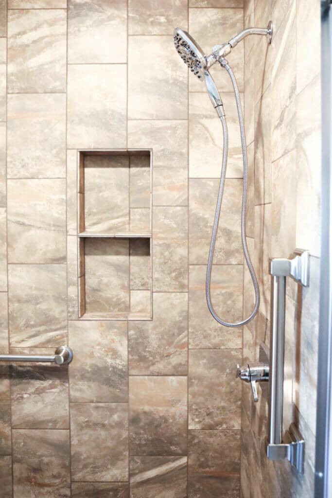 side view of silver shower fixtures (shower head, faucet and handlebars) with large brown marbled tiles along walls