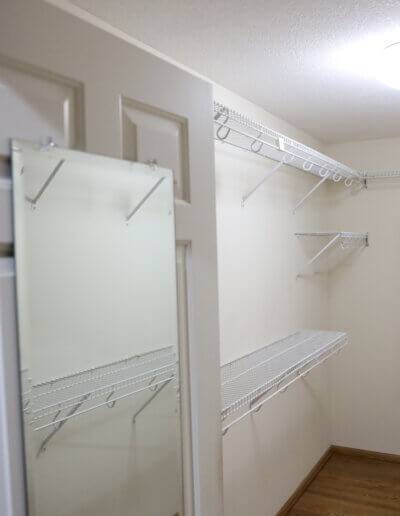 Angled photo of closet facing the door with a full length mirror on it, and white grid racks for hanging and stacking