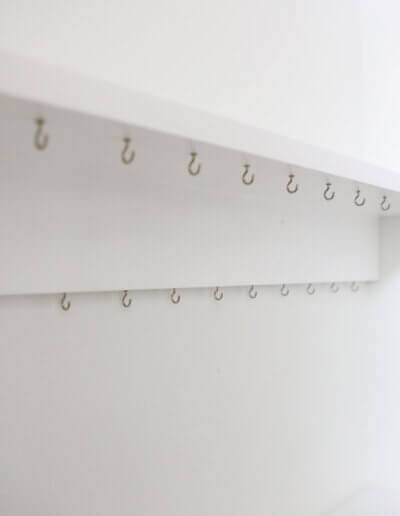 up close image of two white shelves with rows of silver hooks