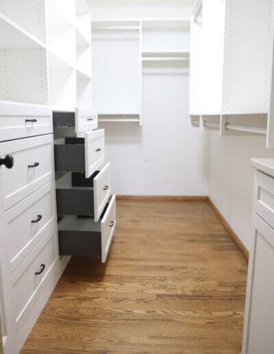 photo into closet from doorframe, showing drawers pulled out on the left side from smallest (at top) to biggest (at bottom). Hardwood floors and trim with white walls and shelving units all around