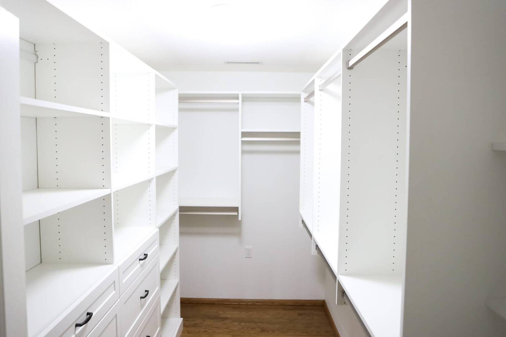 looking into closet of built in white shelving units and cabinets on all three walls