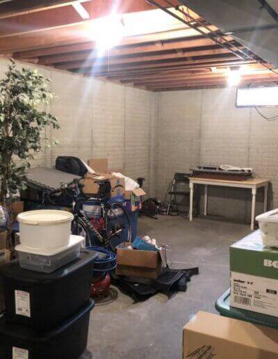 cluttered basement of gray brick walls with boxes, tools and fake plants