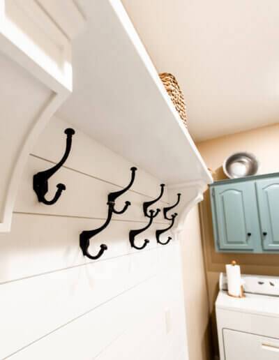 up close photo of black hooks along white wood boards with washer/dryer and teal cabinets in background