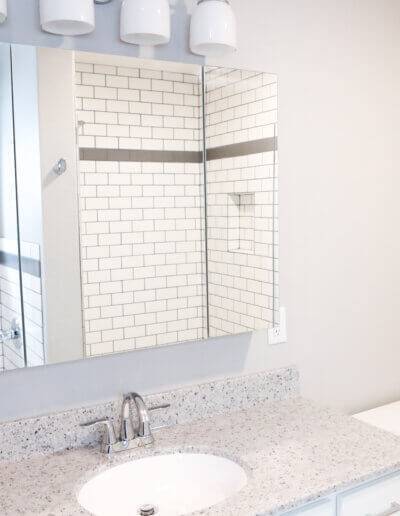 medicine cabinet mirrors above white and gray speckled countertop with small silver faucet. four small white pendants above mirror. white toilet in the corner to the right of the counter.