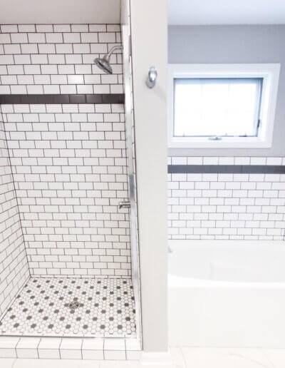 wide shot of black and white subway tiled tub and shower with silver fixtures. Window above bathtub