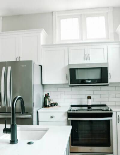 Stainless steel fridge, microwave, and oven next to white cabinets